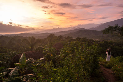 Rear view of woman standing on mountain during sunset