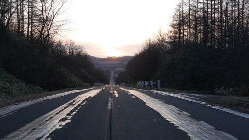 Empty road along trees at sunset