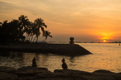 Silhouette birds perching on beach against sky during sunset