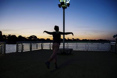 Rear view of silhouette woman standing by railing against sky