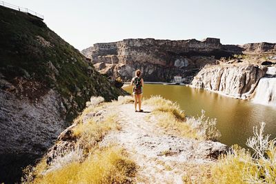 Rear view of young man standing on cliff against clear sky