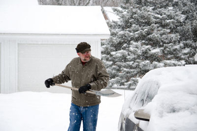 Older man shoveling out car after a snow storm