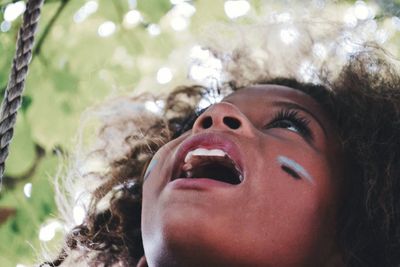 Close-up of girl with mouth open looking up against tree