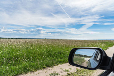 Side-view mirror on field against sky