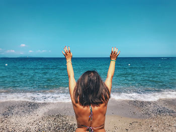 Rear view of woman with arms raised standing at beach