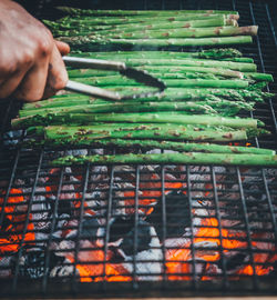 Cropped hand of person preparing asparagus on barbecue grill