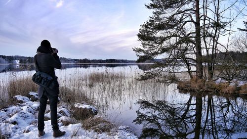 Rear view of man standing by lake against sky during winter