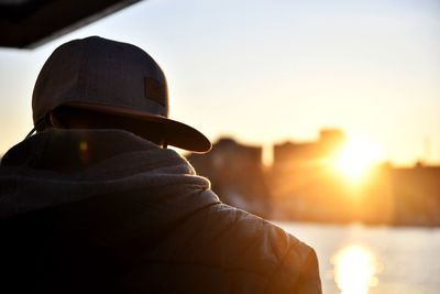 Rear view of man wearing hat against sky during sunset