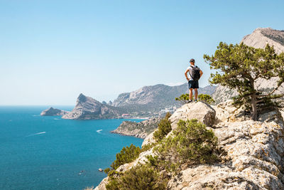 Man on rock by sea against clear sky