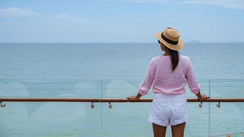 Rear view of woman standing at beach against sky