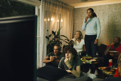 Male teenager with family by sofa watching tv during sporting event at night