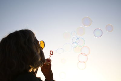 Side view of girl blowing bubbles against clear sky