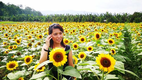 Smiling woman standing amidst sunflowers on field