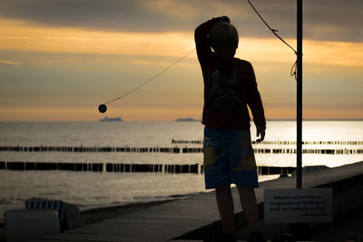 Boy playing with toy at shore against sky during sunset