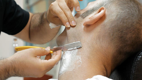 Cropped hands of barber shaving man