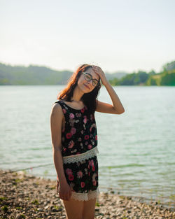 Side view of young woman standing by sea against sky