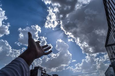 Low angle view of cropped hand against cloudy sky