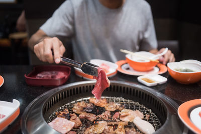 Midsection of man cooking meat on barbecue grill in restaurant