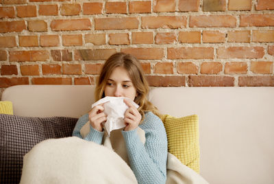 Portrait of a young woman sitting on sofa against brick wall