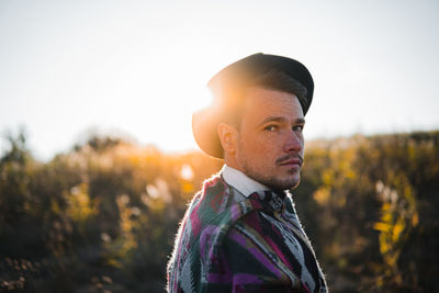 Man in poncho posing against the sun in rural area, looks at camera