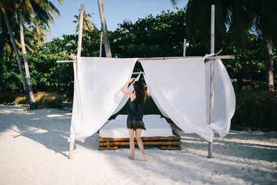 Rear view of woman holding curtain by bed at beach