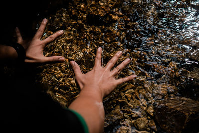 High angle view of hand on rock in shallow water