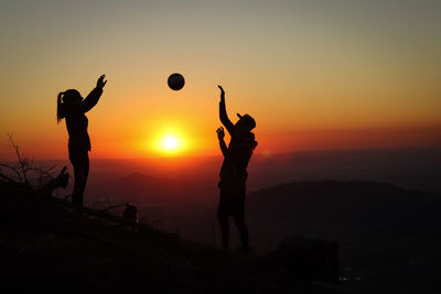 Silhouette people playing soccer against sky during sunset