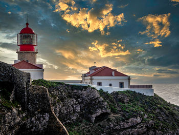 Lighthouse on beach by buildings against sky