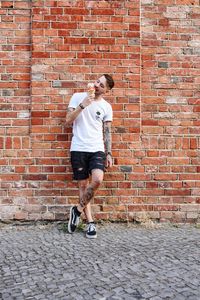 Full length of man eating food while standing against wall