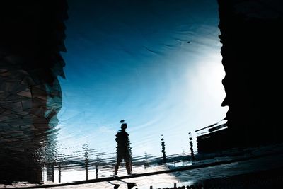 Low angle view of silhouette person standing by building against sky