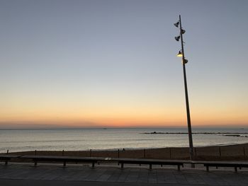 Street light by sea against clear sky during sunset