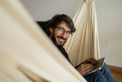 Young man  black glasses working with laptop on a white hammock notebook for working. home office