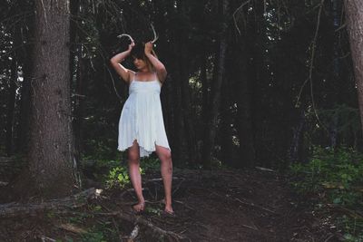 Full length of woman standing by tree trunk in forest