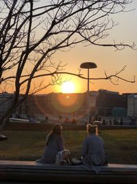 Rear view of couple sitting on bare tree at sunset