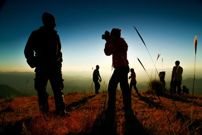 Silhouette people standing on field against sky during sunset