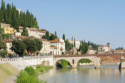 Arch bridge over river by buildings against clear sky