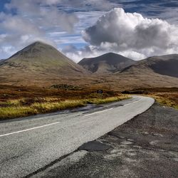 Empty road by mountains against cloudy sky