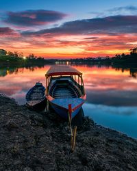 Boat moored on lake against sky during sunset