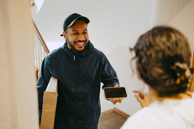 Happy male delivery person giving smart phone to woman for digital signature at doorstep