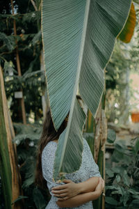 A young woman standing behind a plant leaf