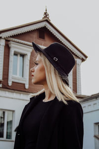 Rear view of woman wearing hat standing against building