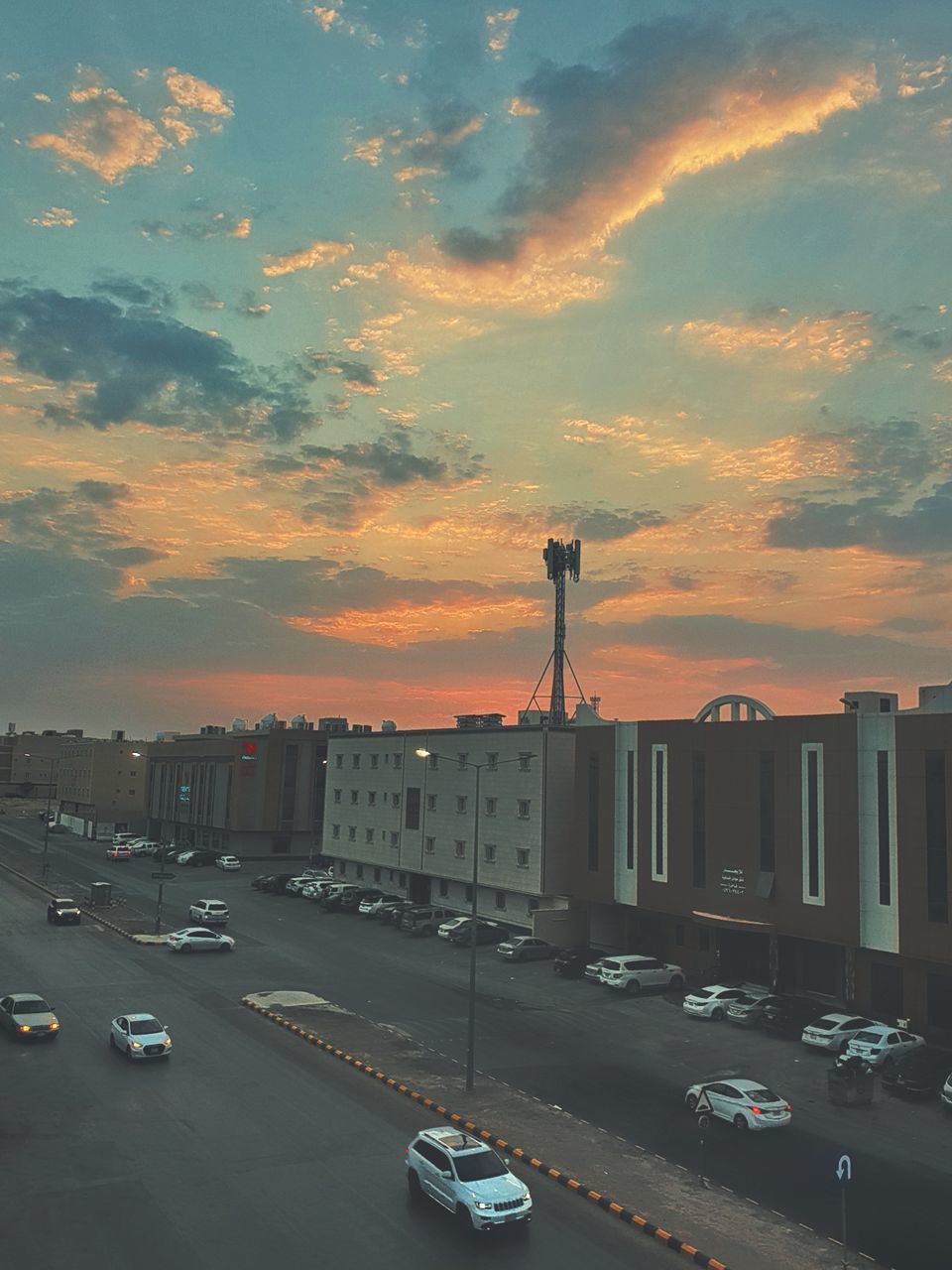 CARS ON ROAD AGAINST BUILDINGS DURING SUNSET