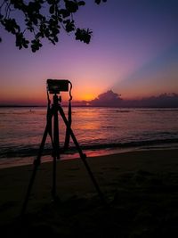 Silhouette camera on beach against sky during sunset