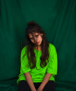 Portrait of young woman with long hair sitting against green fabric