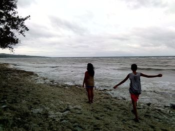 Rear view of men on beach against sky