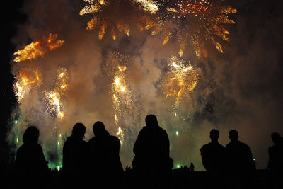 Rear view of silhouette people looking at firework display while sitting outdoors