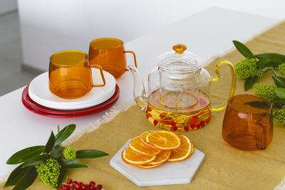 A table setting with orange glass cups, a teapot with tea, fruits and berries.