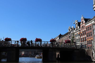 Bridge over river amidst buildings against clear blue sky