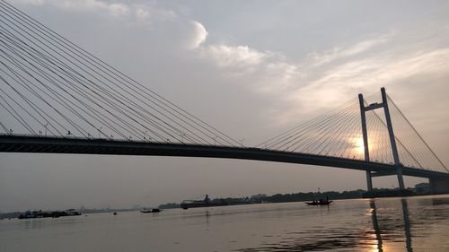 View of suspension bridge over river against cloudy sky