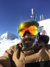 Portrait of man wearing ski goggles against clear blue sky